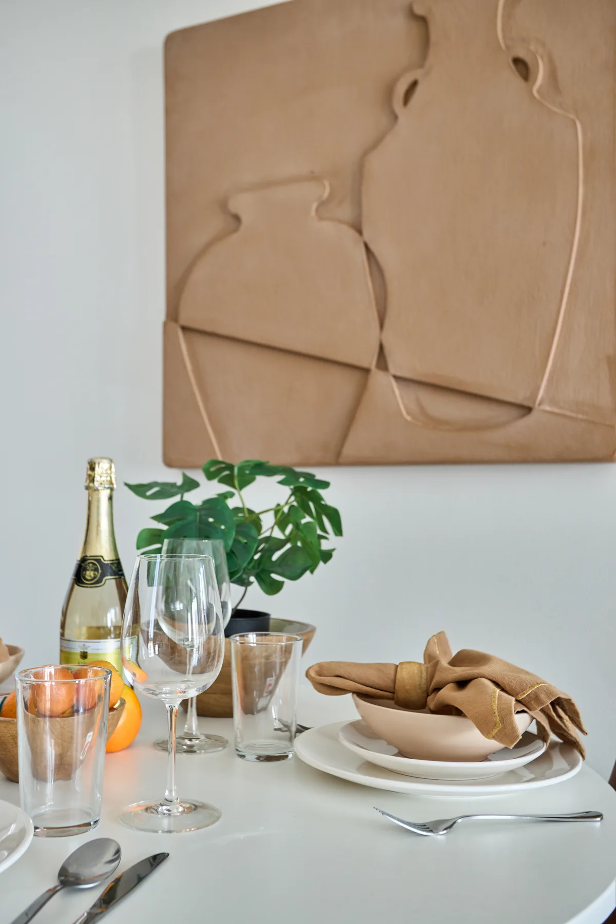 Una mesa de comedor con platos y copas está bajo una obra escultórica en la pared.