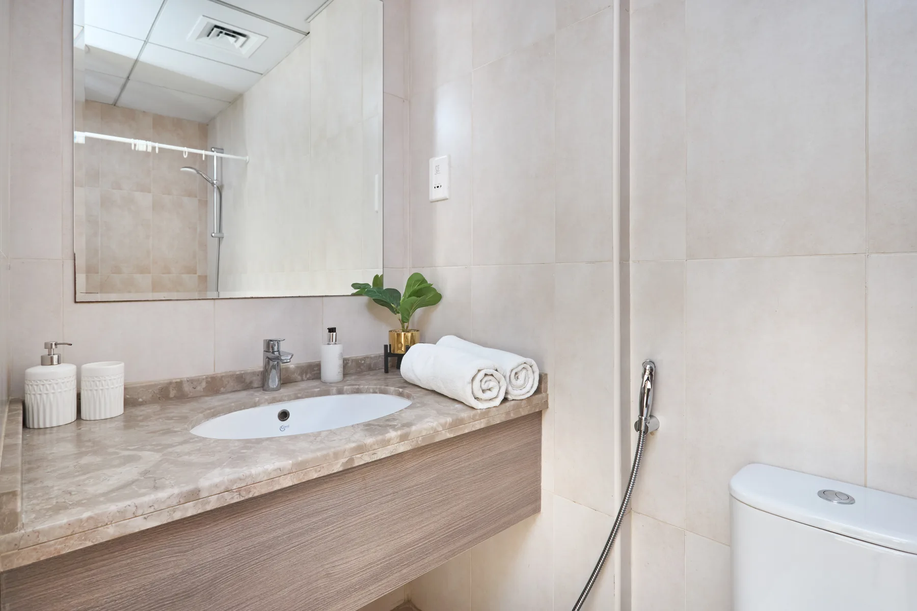 Un tocador de baño con azulejos, espejo, lavabo y ducha de mano.