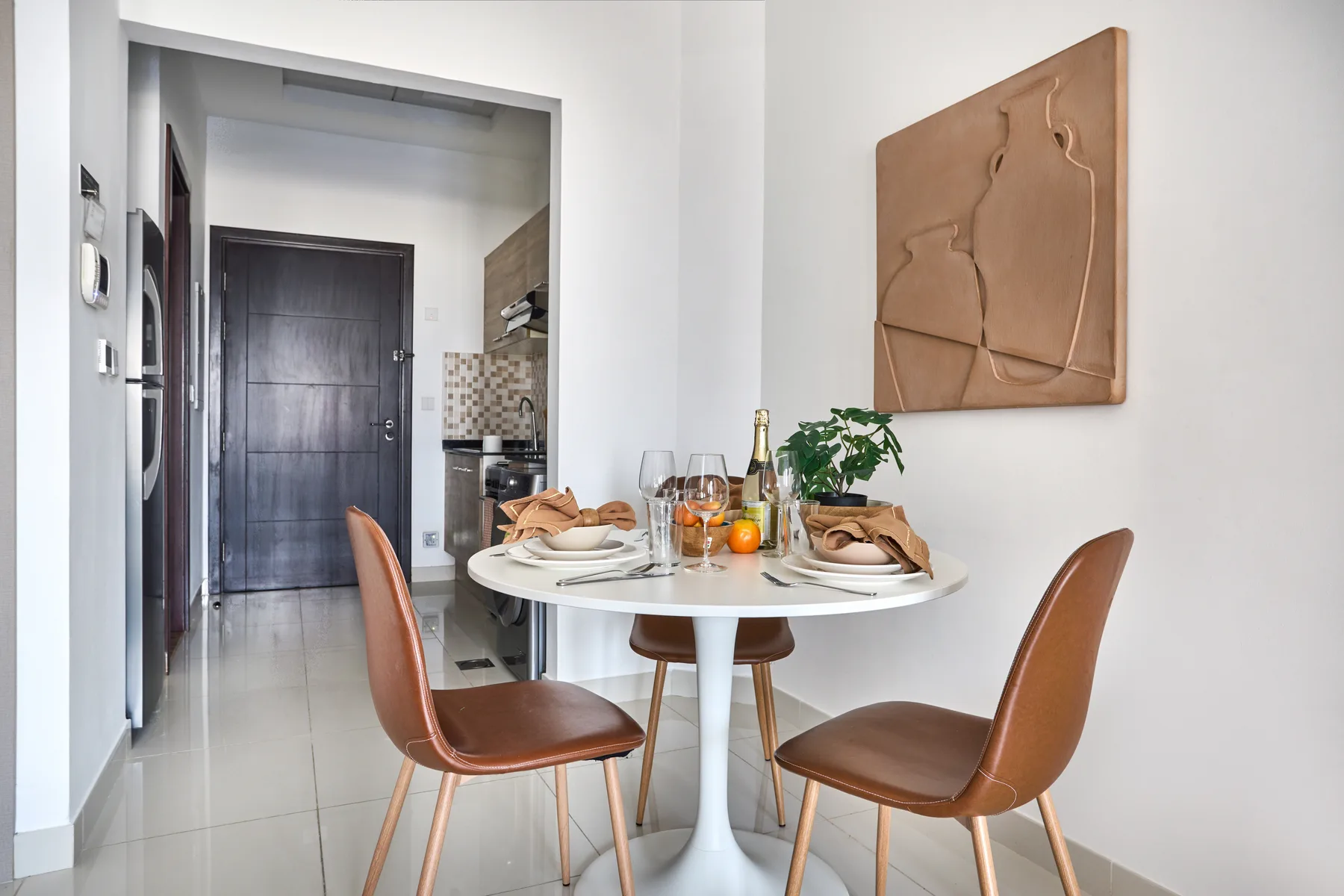 A dining area with a set table and brown seating beside a compact kitchen.