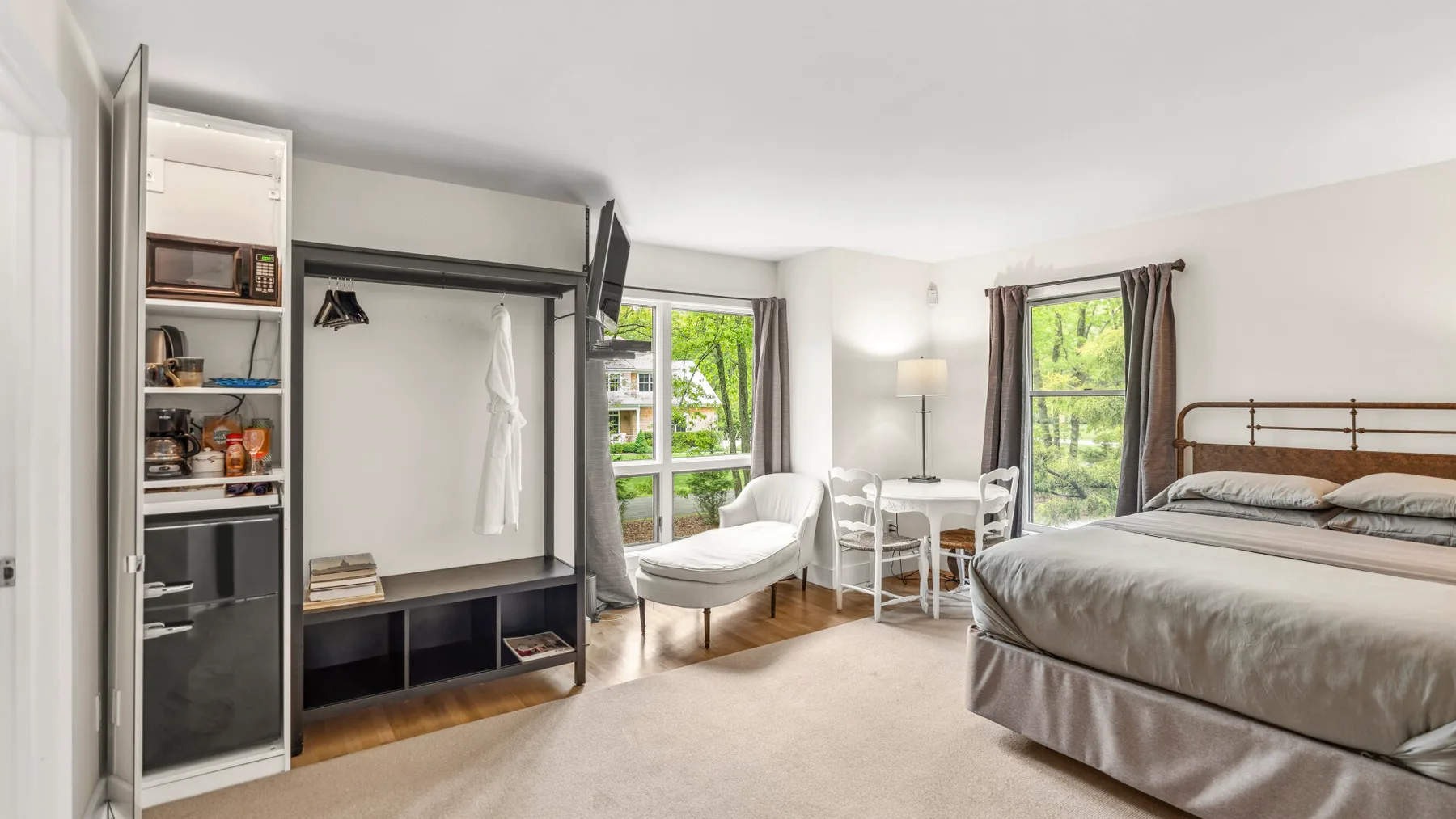 Un dormitorio con una cama, un armario abierto y una pequeña zona de estar junto a las ventanas.