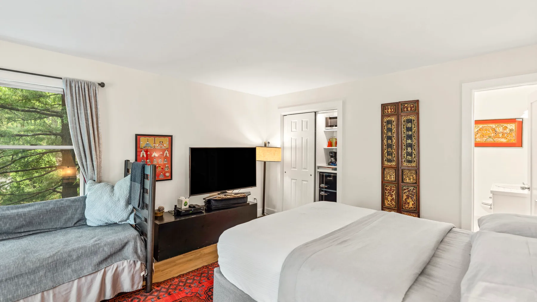 Un dormitorio con una cama grande, un televisor y una ventana con vista a los árboles.