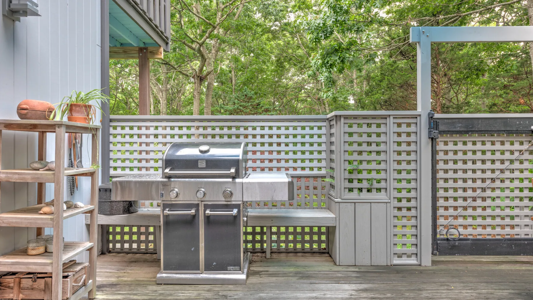 Una terraza exterior con una parrilla de acero inoxidable junto a una valla de celosía.