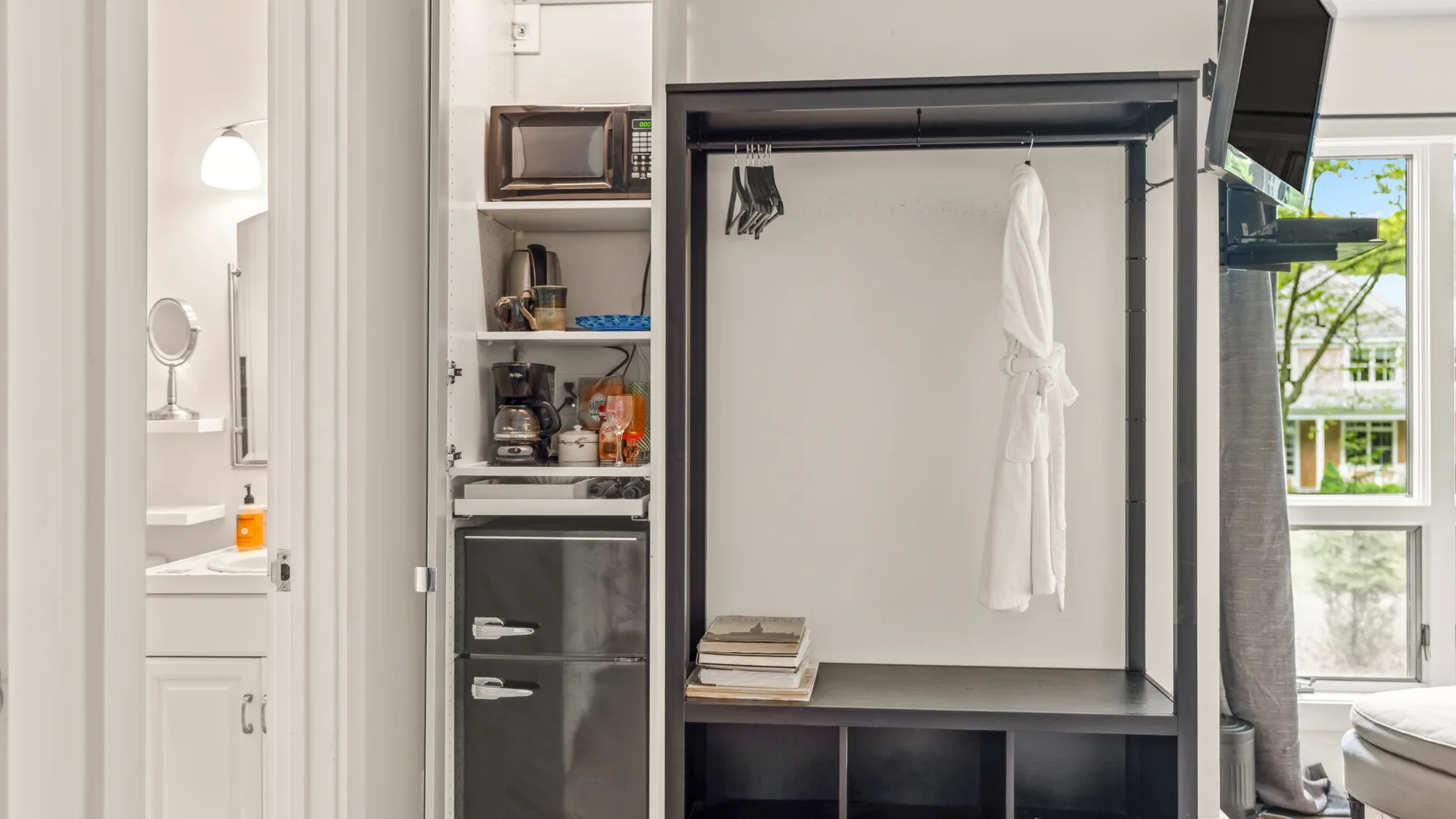 Un dormitorio con un armario abierto y una ventana luminosa junto a la cama.