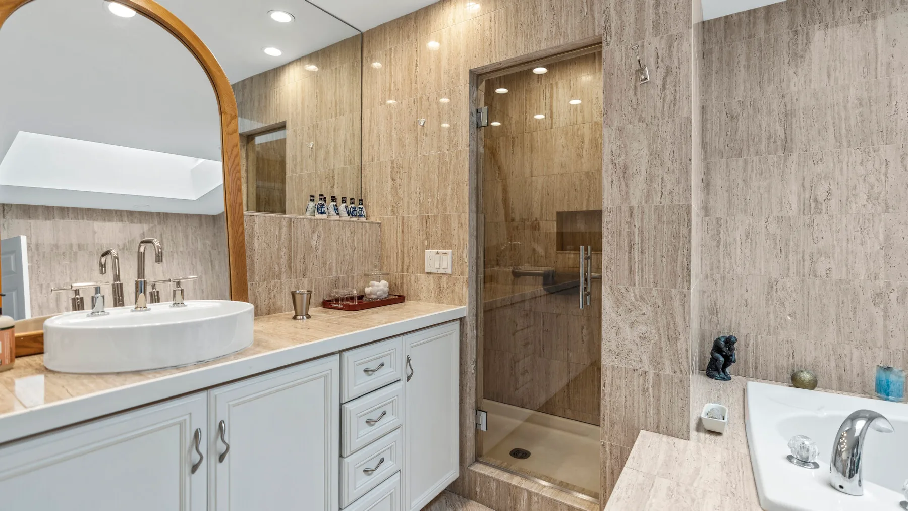 Baño luminoso con un mueble de lavabo largo, espejos y una ducha de vidrio.