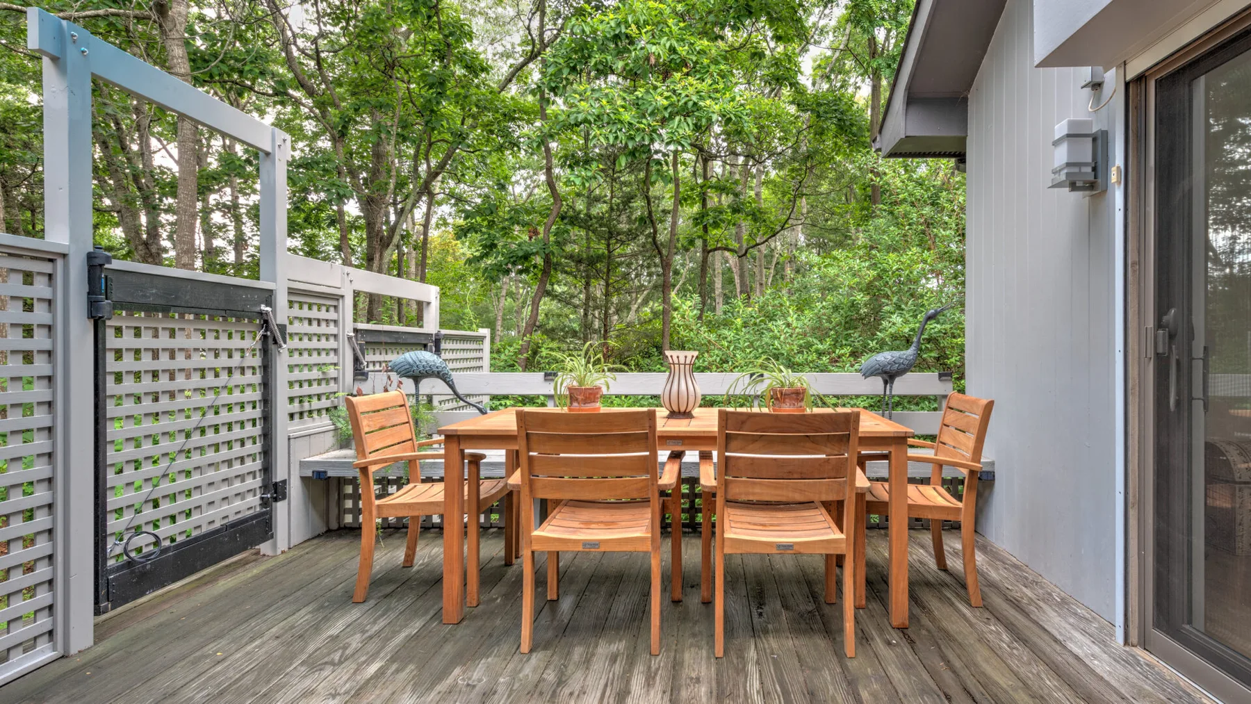 Una zona de comedor al aire libre con asientos de madera, una mesa y árboles al otro lado de la cerca.