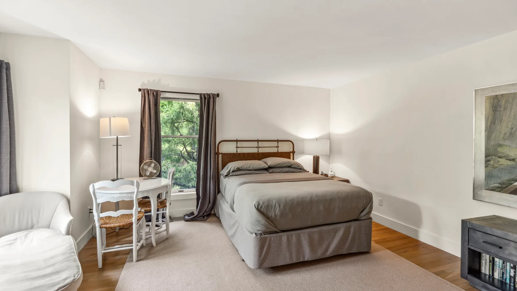 Un dormitorio con una cama tendida, mesitas de noche y un pequeño escritorio junto a la ventana.