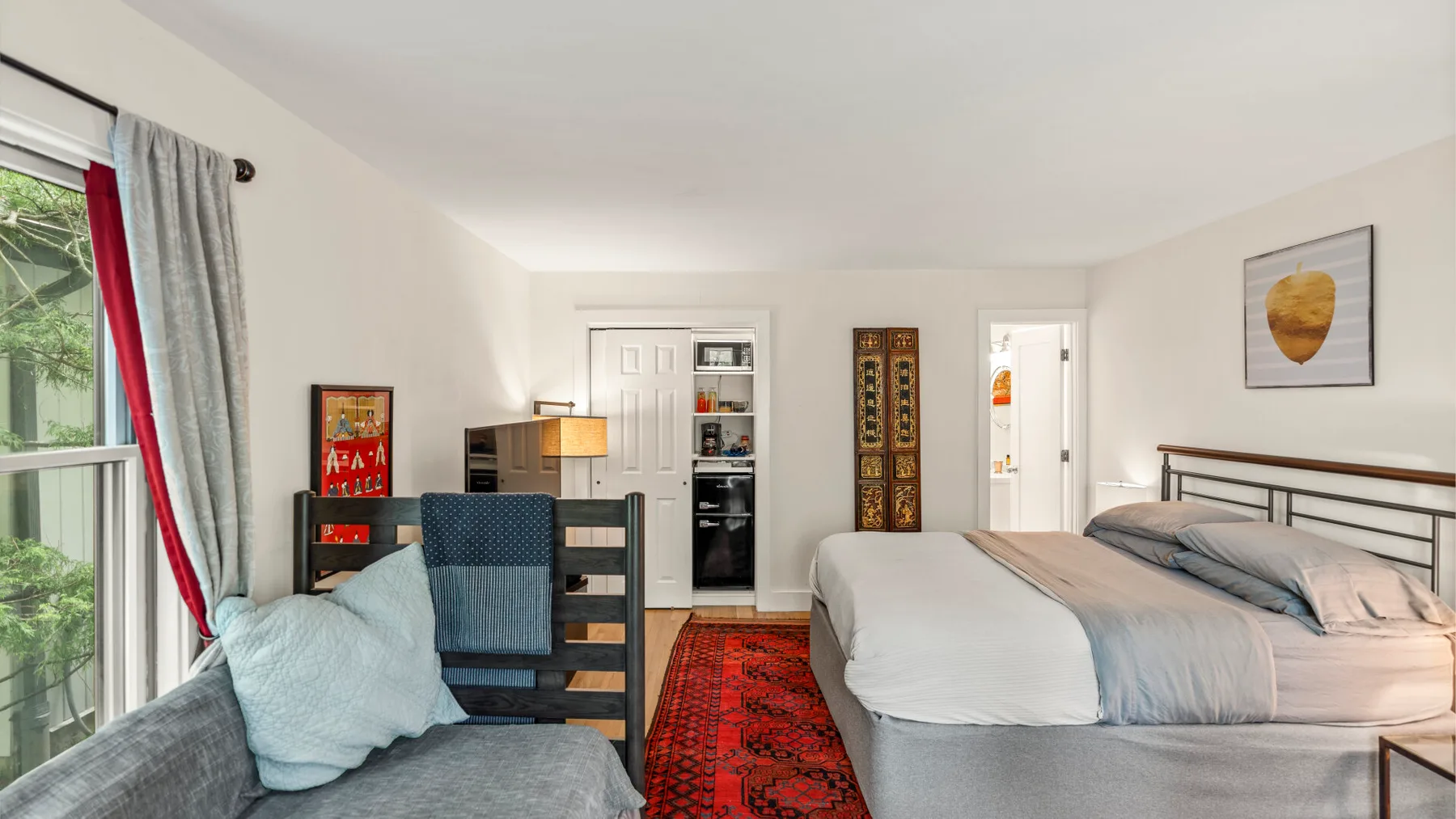 Un dormitorio luminoso con una cama grande, una alfombra roja estampada y un escritorio.