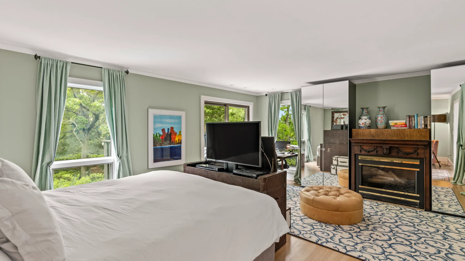 Un dormitorio con cama, televisor y ventanas con vistas a la vegetación.