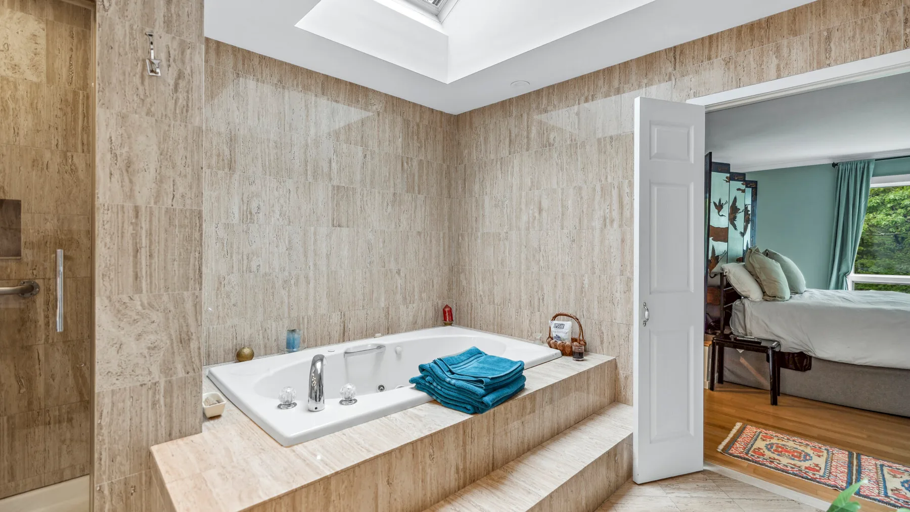 Un baño con paredes revestidas tiene una bañera junto a una puerta abierta hacia un dormitorio.
