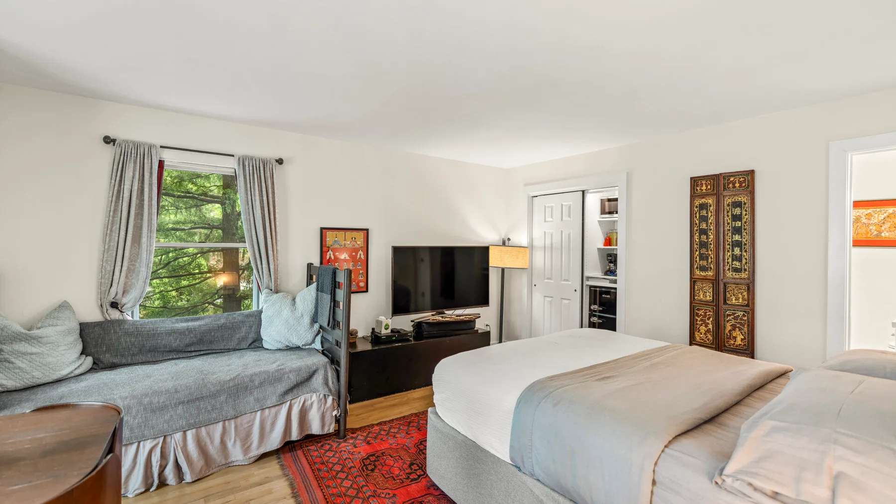Un dormitorio con una cama grande, un televisor y un diván junto a la ventana.