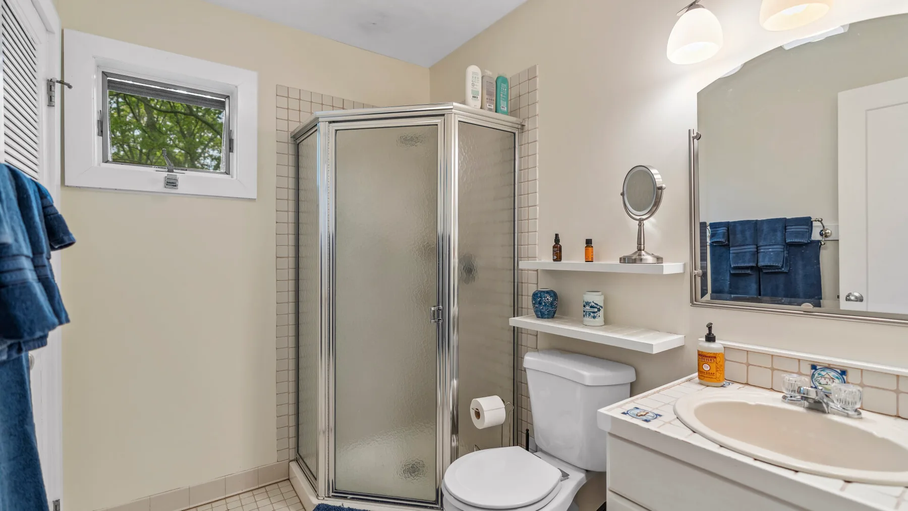 Un baño con ducha, inodoro y lavabo bajo un espejo grande.