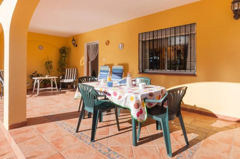 A sunny outdoor dining area with a table, chairs, and bright orange walls.