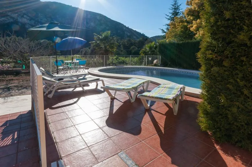 An outdoor pool beside a tiled patio with lounge chairs and mountain views.