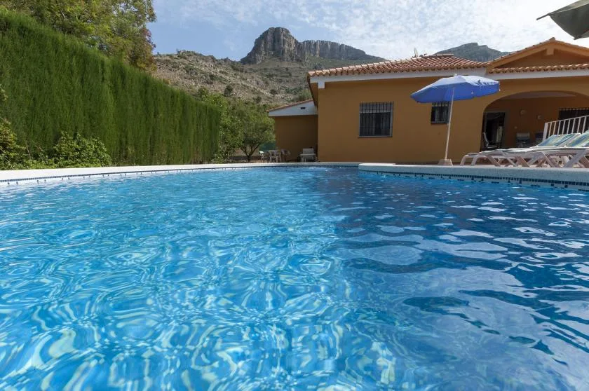 A swimming pool sits beside a house, with a mountain rising in the background.