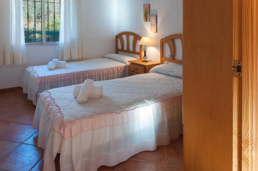 A bedroom with two beds, a bedside table, and a window.