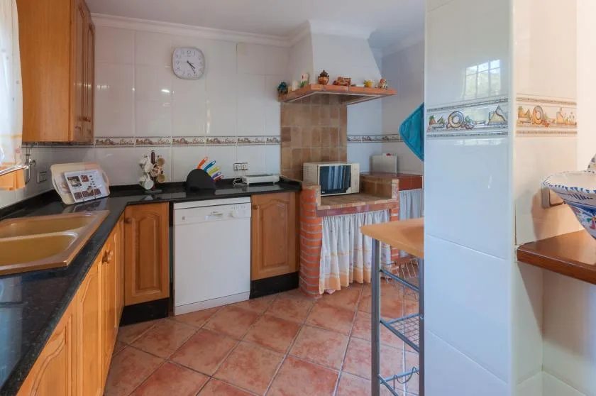 A tiled kitchen with wooden cabinets, a countertop, and a small television.