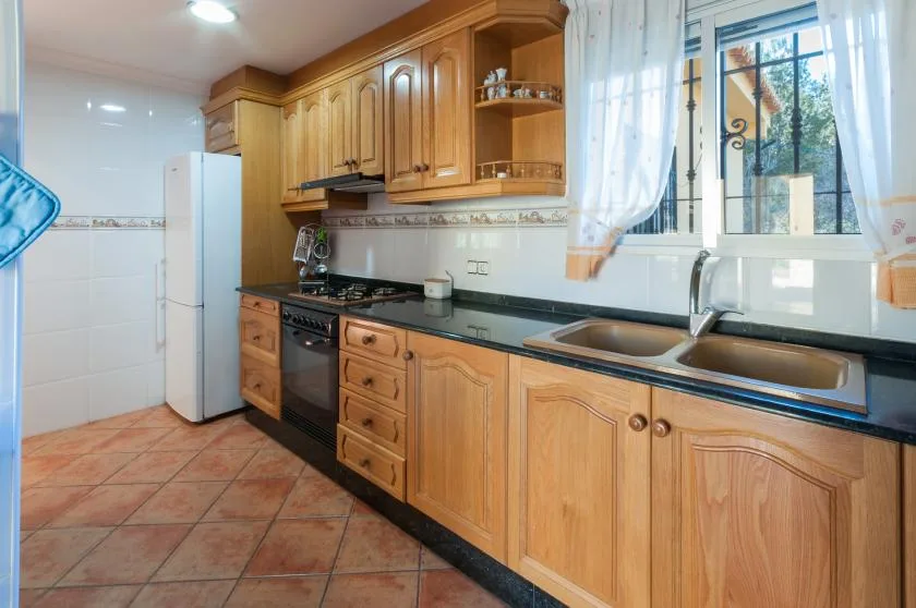 A kitchen with wooden cabinets, a refrigerator, and a sink beneath a window.