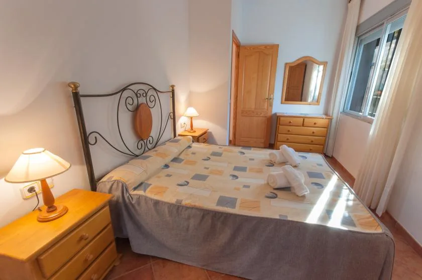 A bedroom with a double bed, bedside tables, and a dresser beneath a mirror.