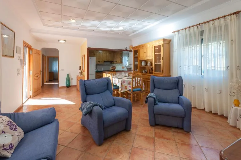 A living area with blue seating, a dining table, and a kitchen in the background.