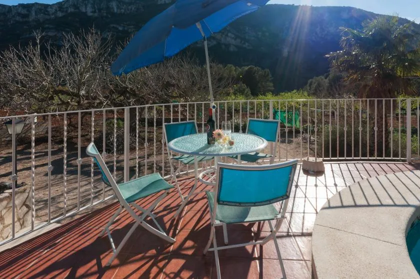 An outdoor patio has a table and seating beneath a blue umbrella.