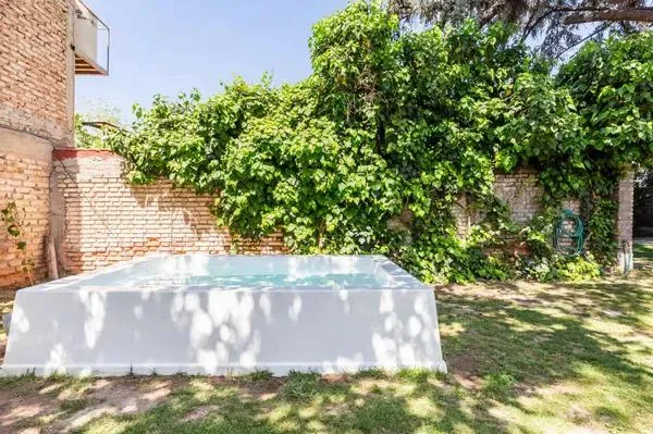 Una piscina blanca al aire libre está en un jardín frondoso junto a una pared de ladrillo.