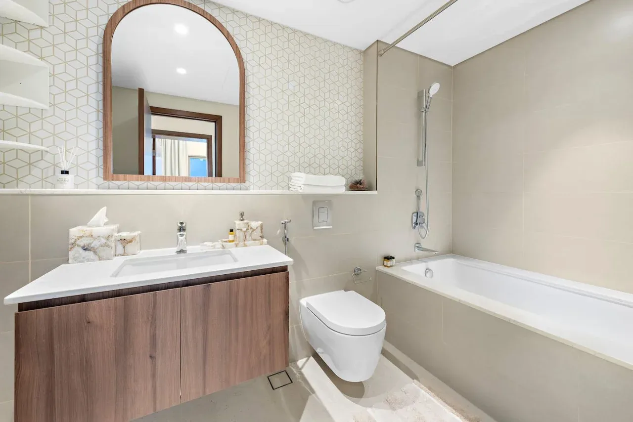 Un baño luminoso con lavabo, inodoro y bañera bajo una ducha.