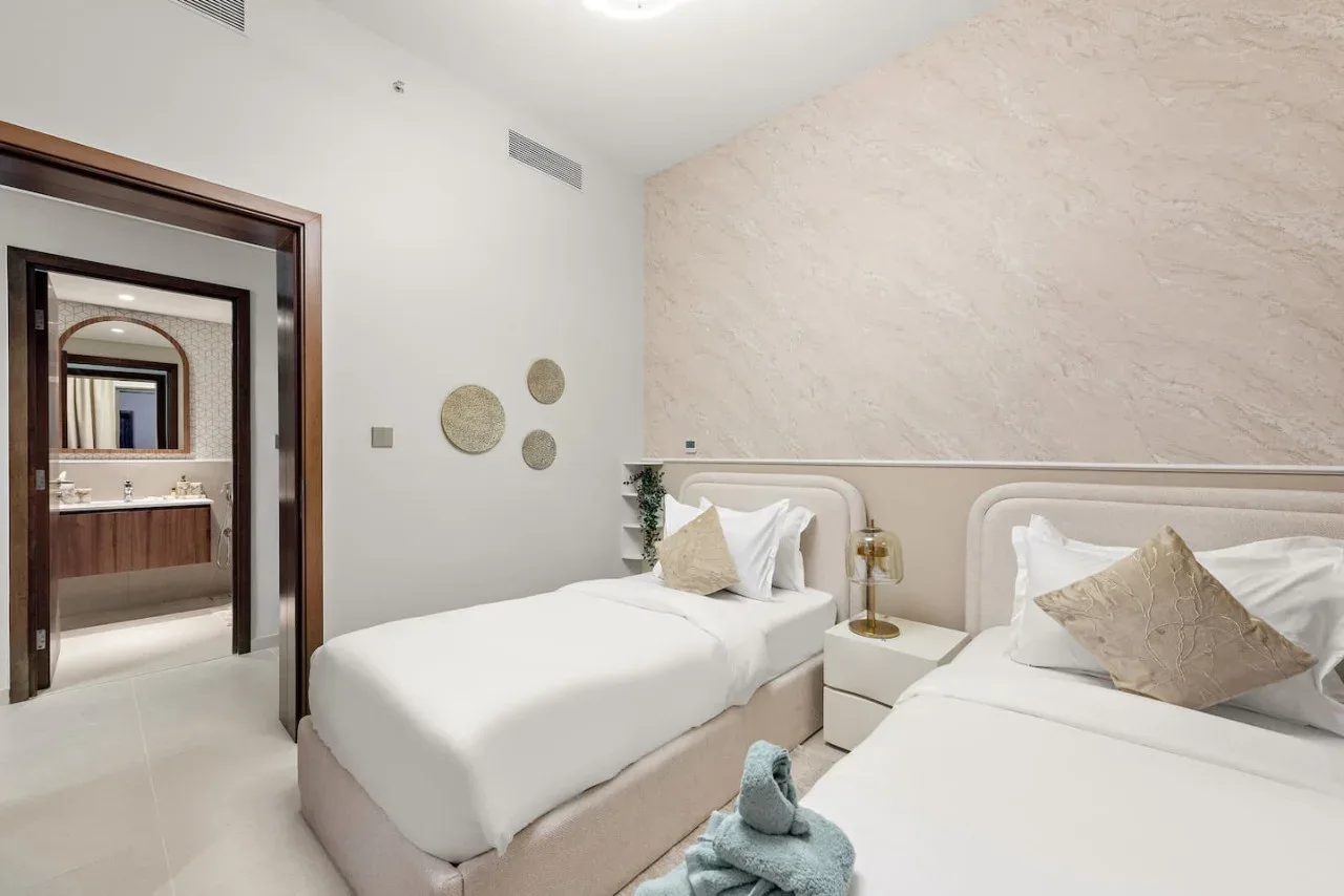 Un dormitorio luminoso con dos camas y una pared decorativa de textura clara.