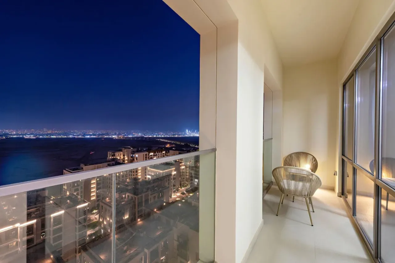 Un balcón de noche ofrece vistas de edificios iluminados y una extensión de agua.