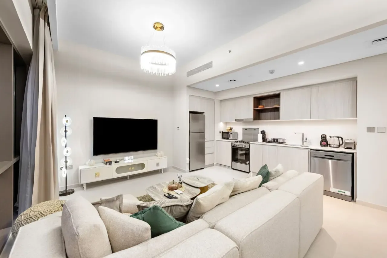Una sala luminosa con asientos frente a un televisor y una cocina abierta.