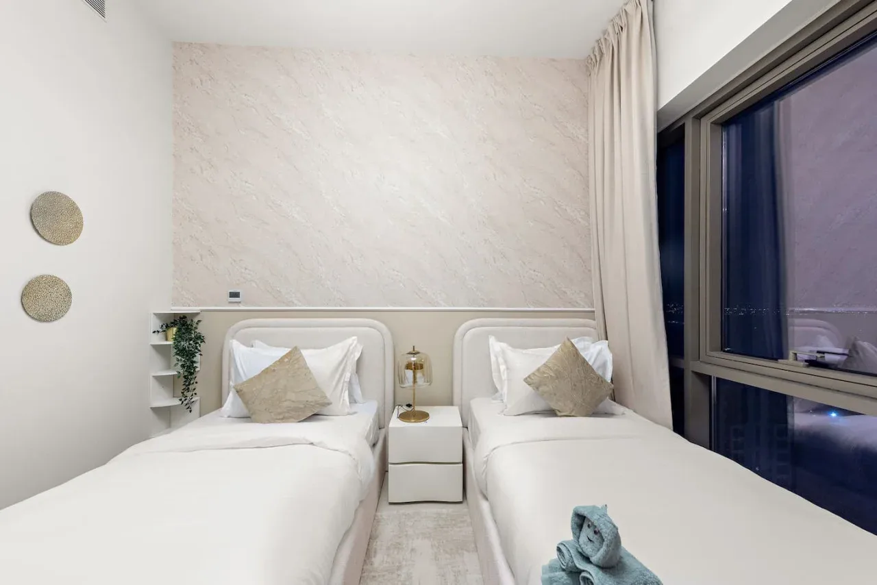 Un dormitorio luminoso con dos camas bien hechas junto a una ventana grande.