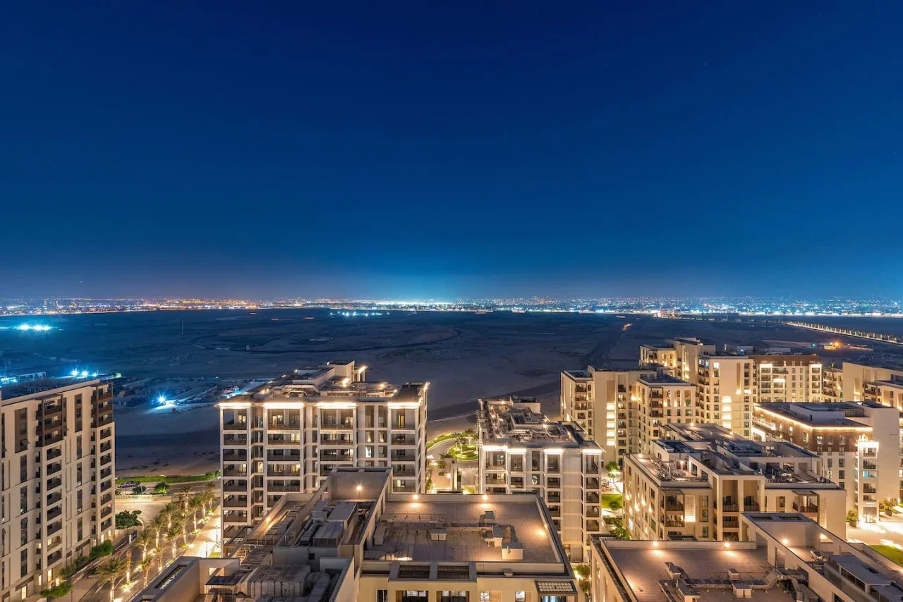 Un paisaje urbano nocturno muestra edificios de apartamentos iluminados bajo un cielo azul oscuro.