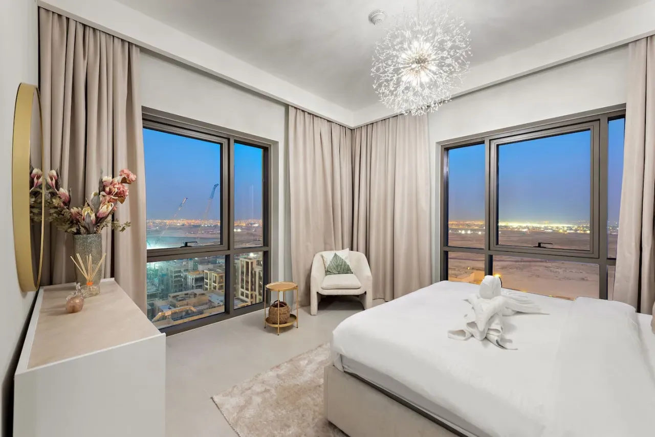 Un dormitorio con una cama grande, ventanas altas y cortinas con vistas a la ciudad.