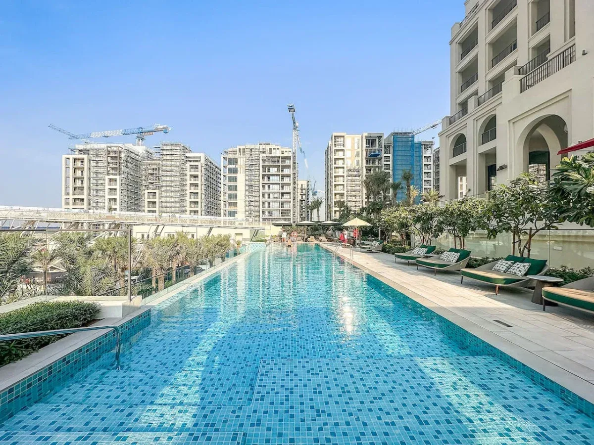 Una piscina al aire libre junto a un edificio moderno, con tumbonas en la terraza.