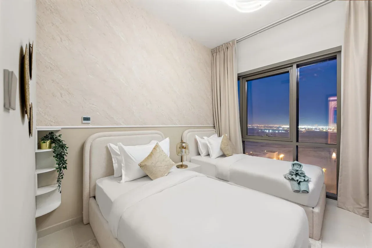 Un dormitorio con dos camas junto a una gran ventana con vistas a las luces de la ciudad.