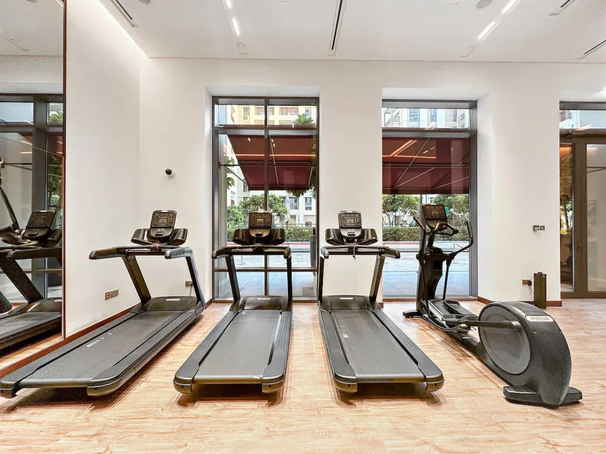 Un gimnasio luminoso con cintas de correr y equipo de ejercicio junto a grandes ventanas.