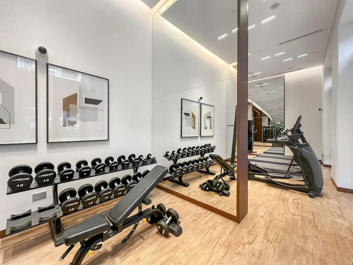 Un gimnasio con filas de mancuernas, un banco de ejercicio y cintas de correr.