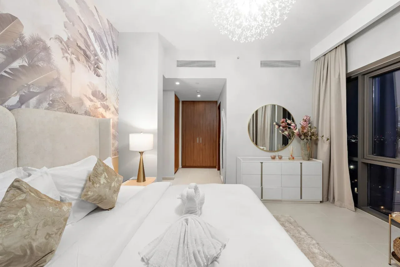 Un dormitorio luminoso con una cama, una lámpara de noche y una cómoda junto a la ventana.