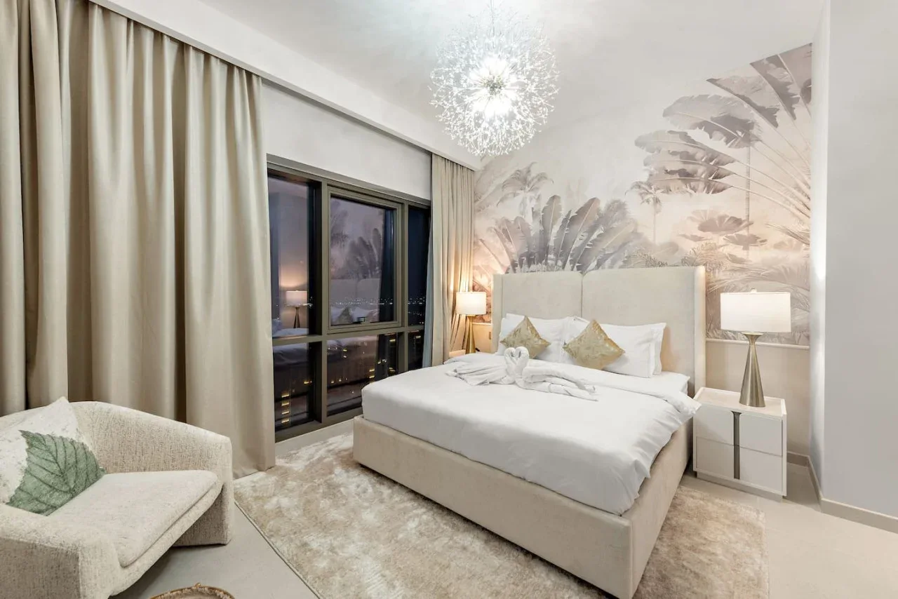Un dormitorio con una cama, mesitas de noche y una ventana grande enmarcada por cortinas.