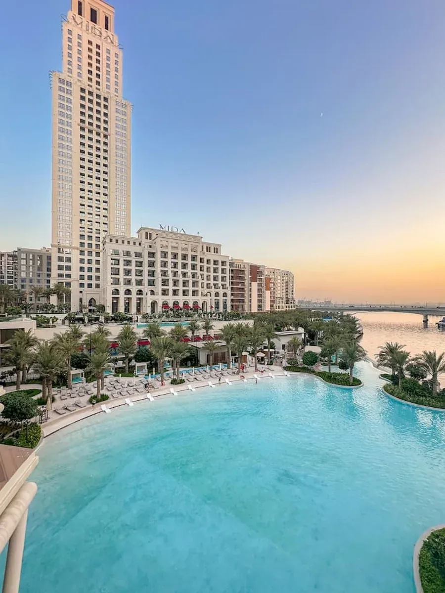 Una gran piscina al aire libre junto a un hotel frente al agua al atardecer.