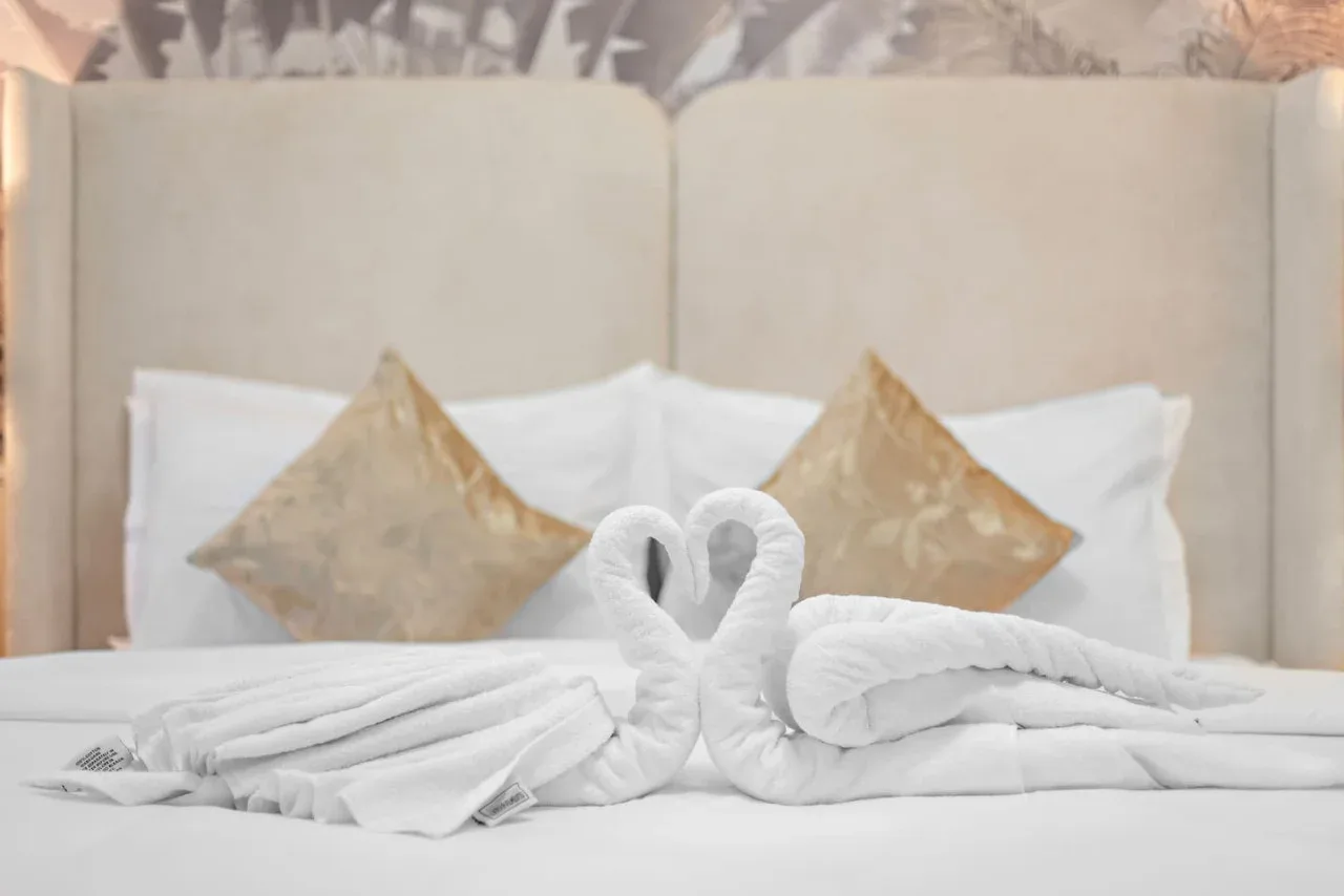 Una cama bien arreglada muestra toallas blancas dobladas en forma de cisne.