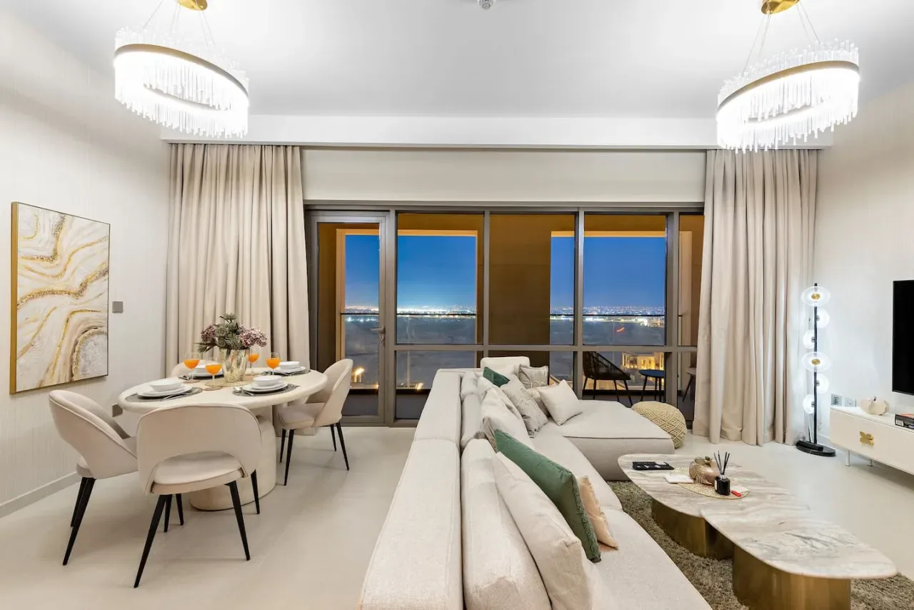 A bright living room with a dining table beside large windows overlooking the city.