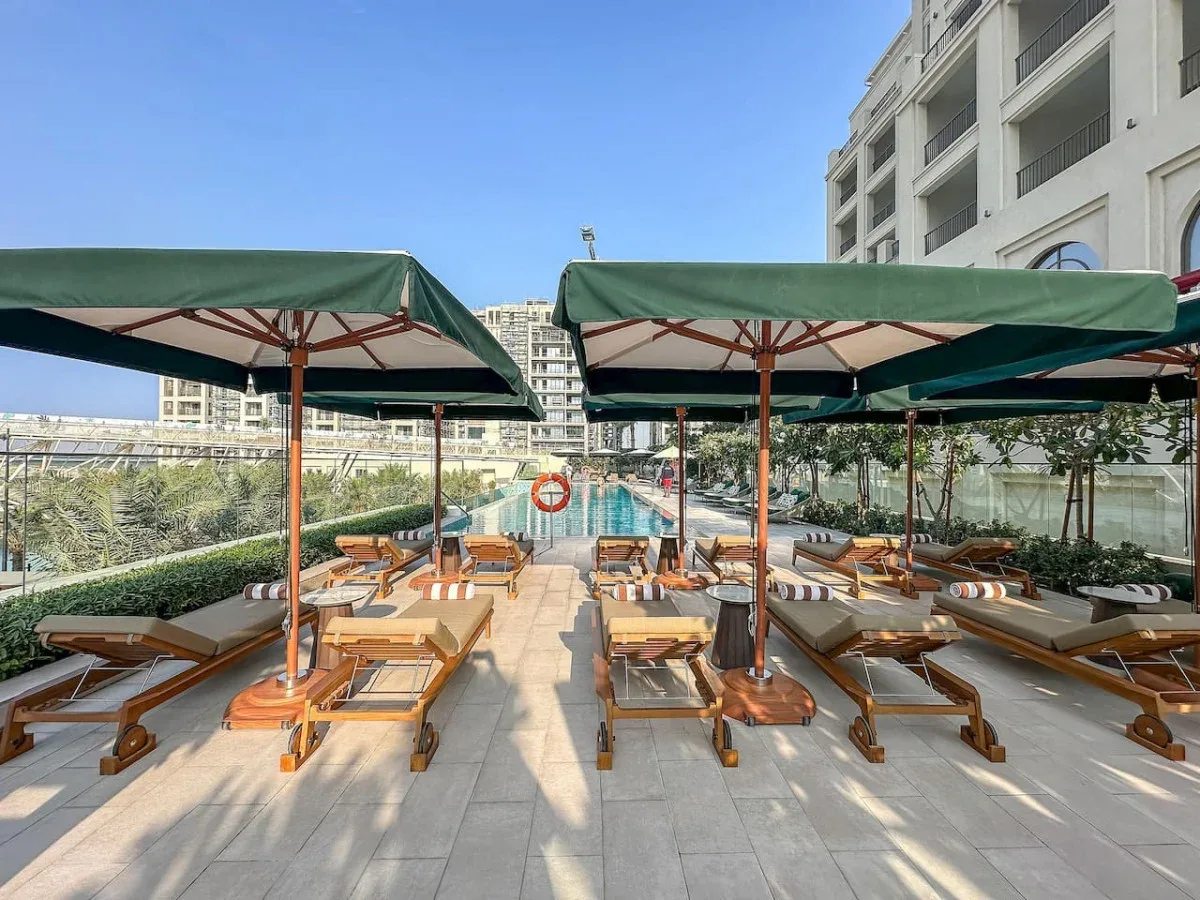 Una terraza junto a la piscina con asientos bajo grandes sombrillas verdes.