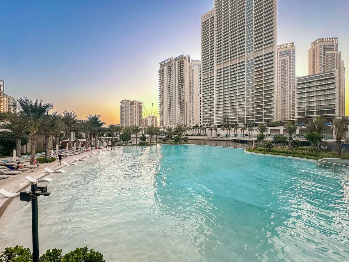 Una gran piscina al aire libre está rodeada de palmeras y edificios altos.