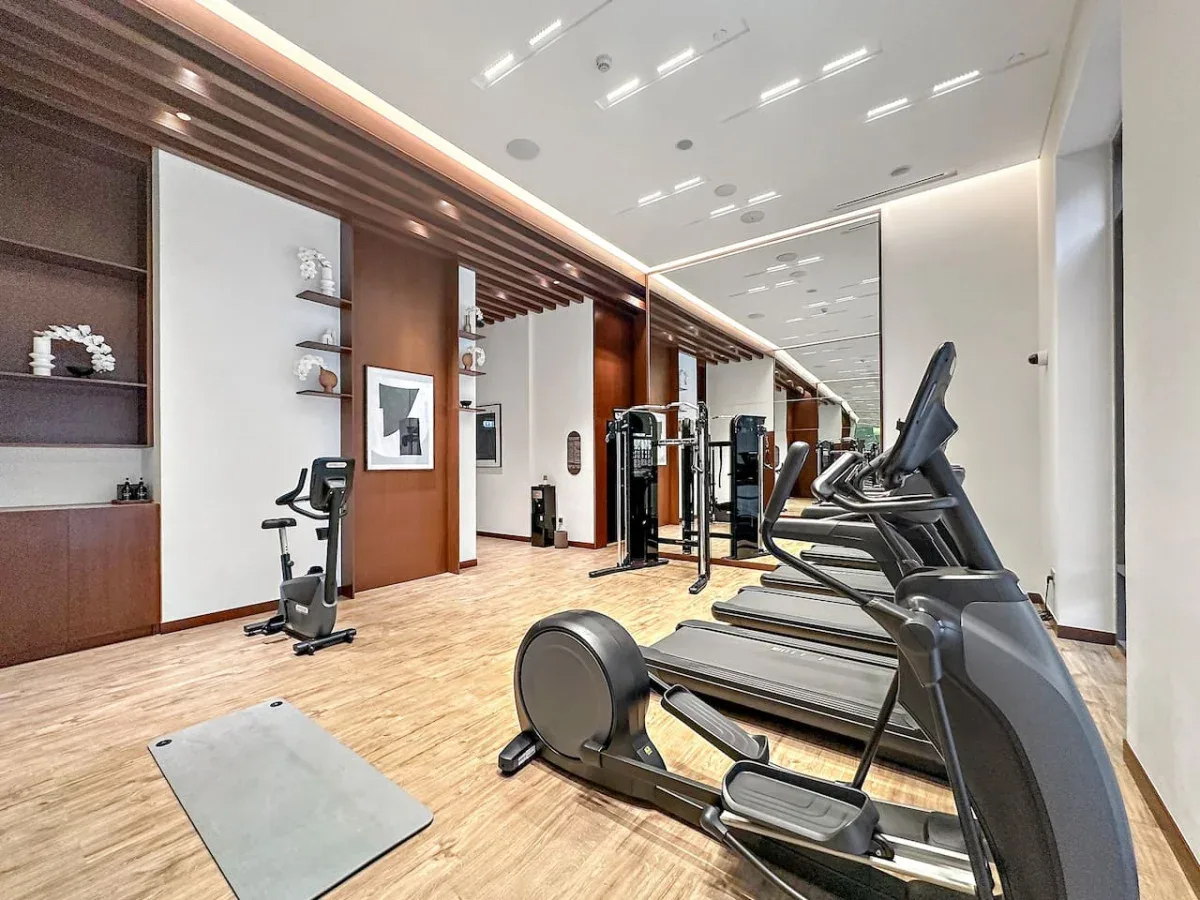 Un gimnasio con cintas de correr, bicicletas estáticas y una colchoneta en el suelo.