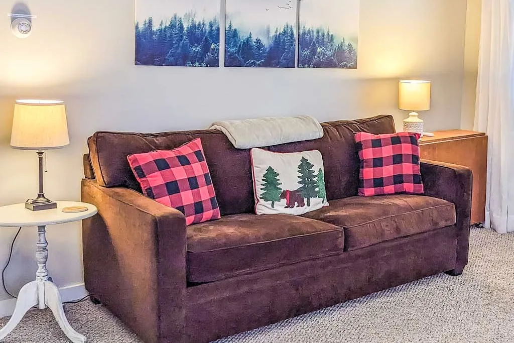 A living room with a brown sofa and forest artwork above it.