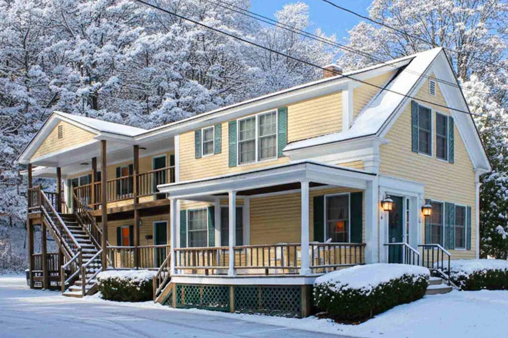 A yellow multi-story house with porches stands among snow-covered trees.