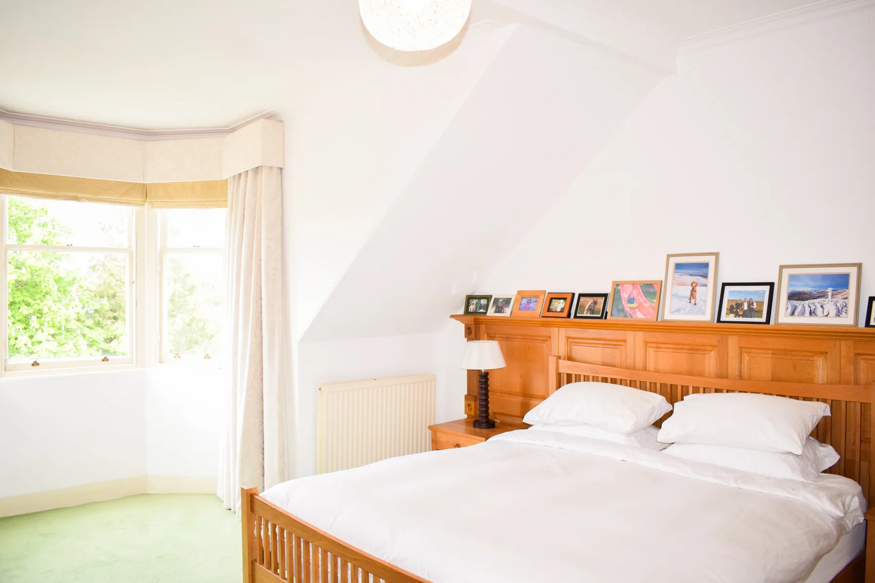 A bright bedroom with a wooden bed beneath framed pictures.