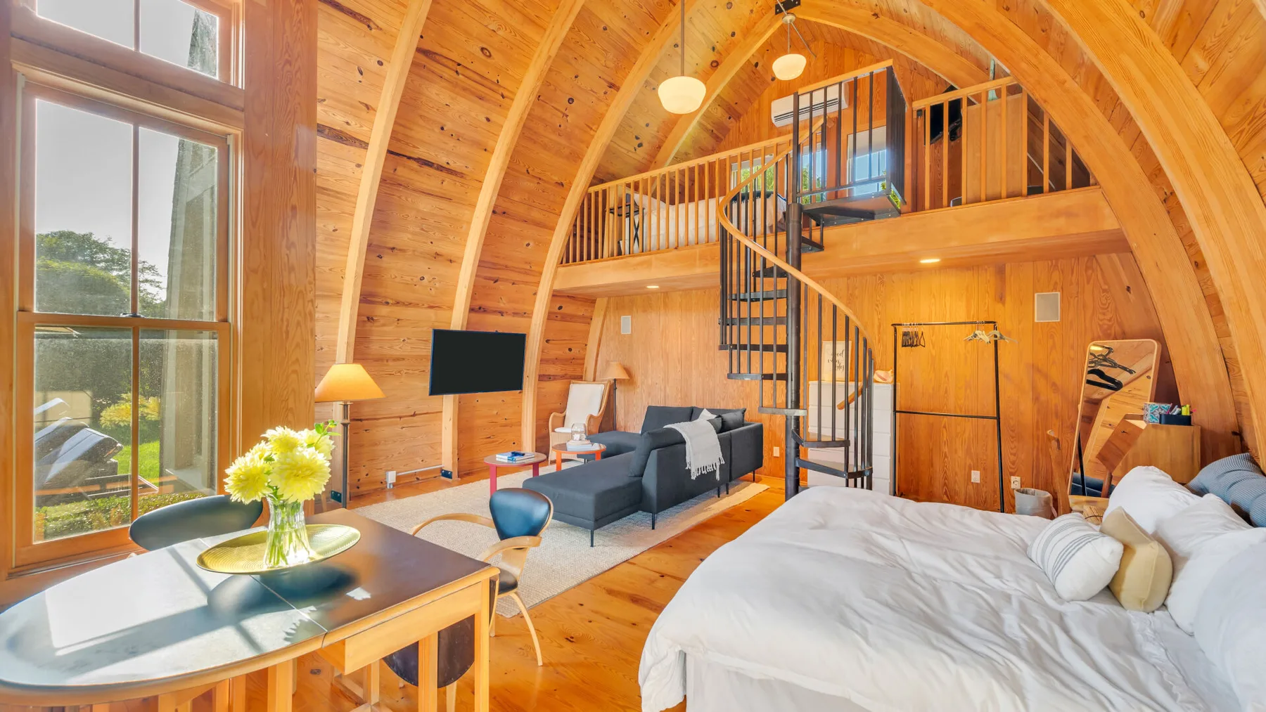 Un dormitorio revestido de madera con una cama grande, una zona de estar y una escalera de caracol.