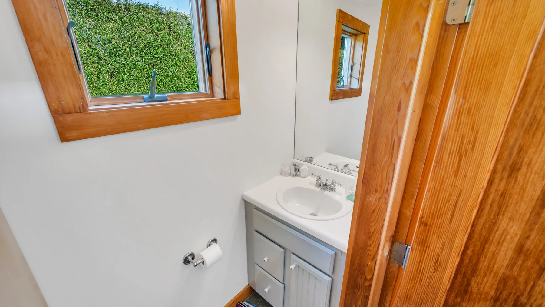 Un lavabo de baño está junto a una ventana y una puerta de madera.