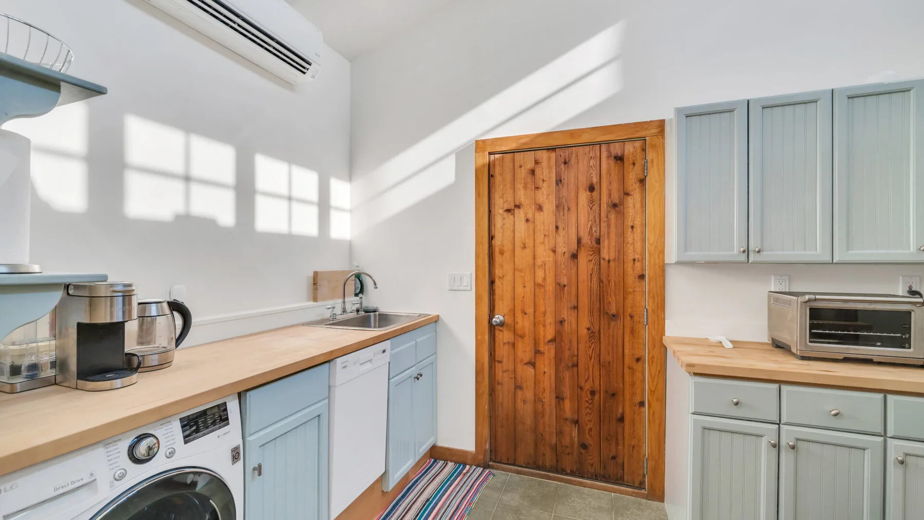 Una cocina luminosa con gabinetes claros, encimeras de madera y una puerta de madera.
